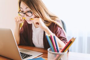 A woman bites her pencil in frustration as she stares at her computer screen