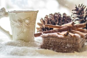 a glass mug, a pile of cinnamon sticks, and a couple pine cones rest in the snow