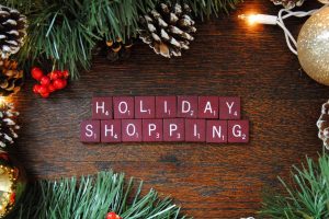 "Holiday shopping" spelled out with Scrabble letters on a table with pine cones and ornaments