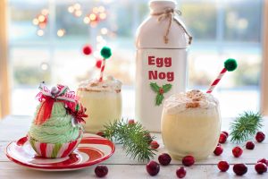 two cups of eggnog, next to a bottle of eggnog and a Christmas cupcake