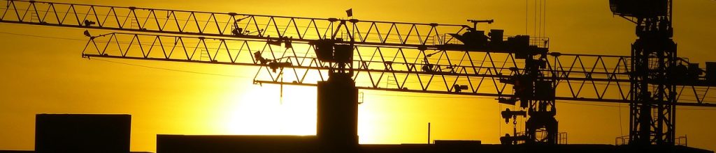 construction cranes silhouetted against the setting sun