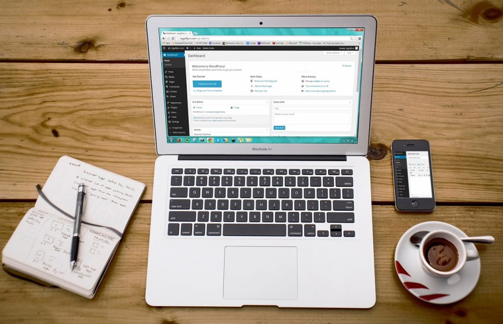 a laptop on a desk with a notebook and cup of coffee