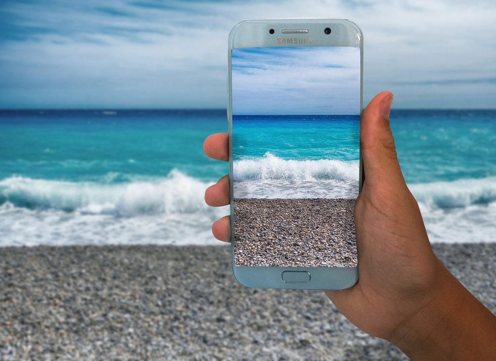hand holding up a phone, taking a picture of the beach